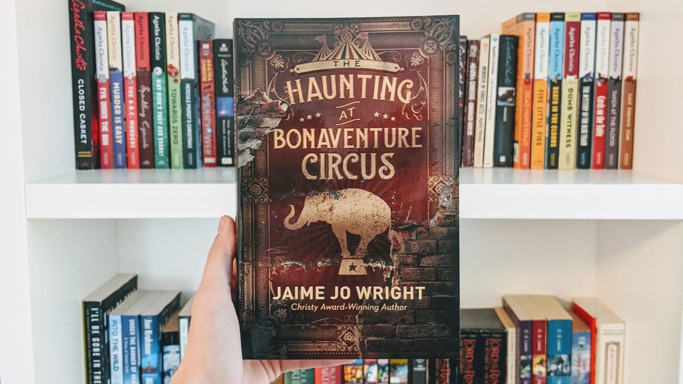 The Haunting at Bonaventure Circus book cover in front of white bookshelf filled with books