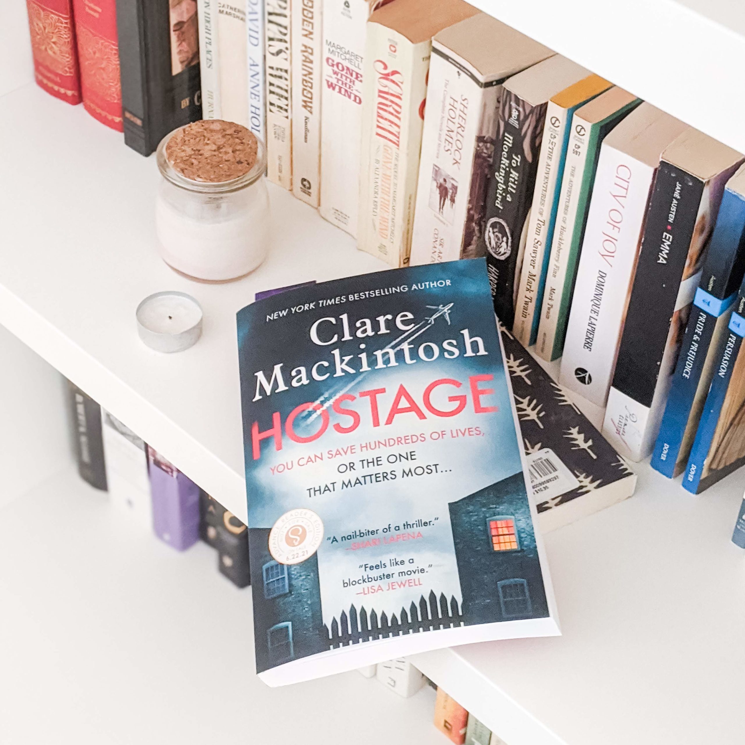 Hostage by Clare Mackintosh -- book lying on a white bookshelf beside books