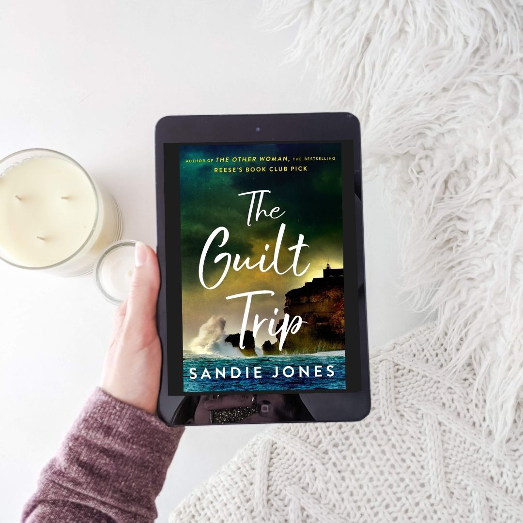 The Guilt Trip by Sandie Jones, book on e-reader set against white background with pillows and candles